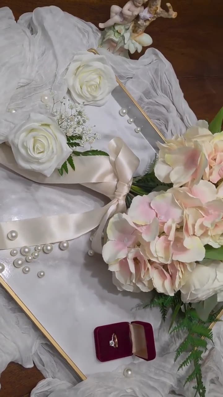 Blush hydrangea and cream rose bridal bouquet styled on ivory silk with scattered pearls, a gold-edged tray and an open ring box