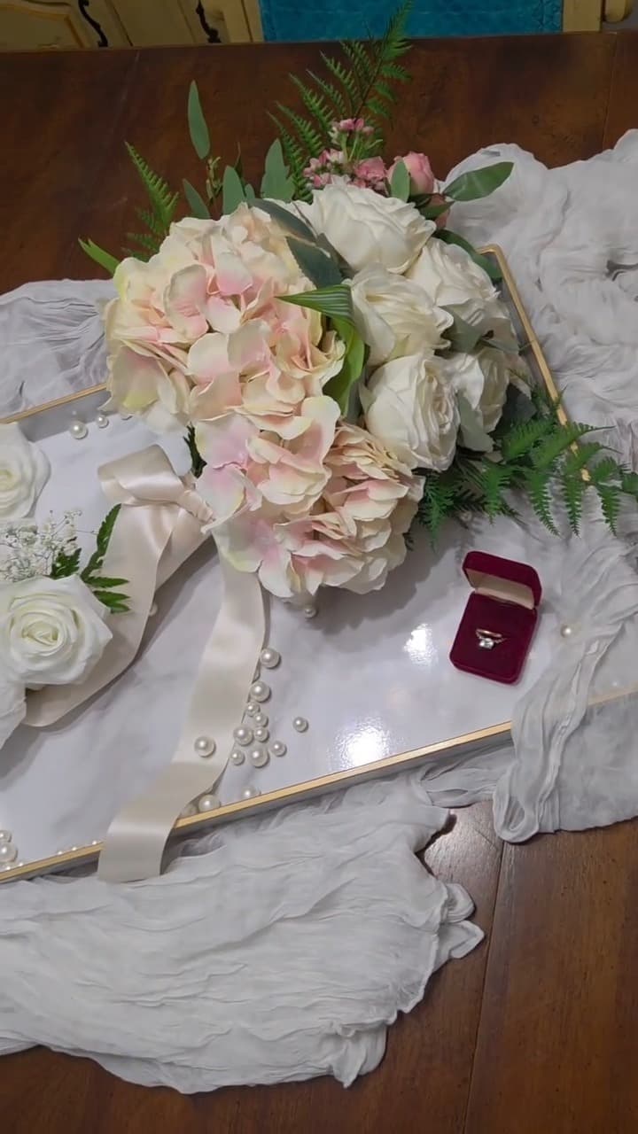 Bridal flat lay with blush bouquet, gauze runner, pearls and a ring box